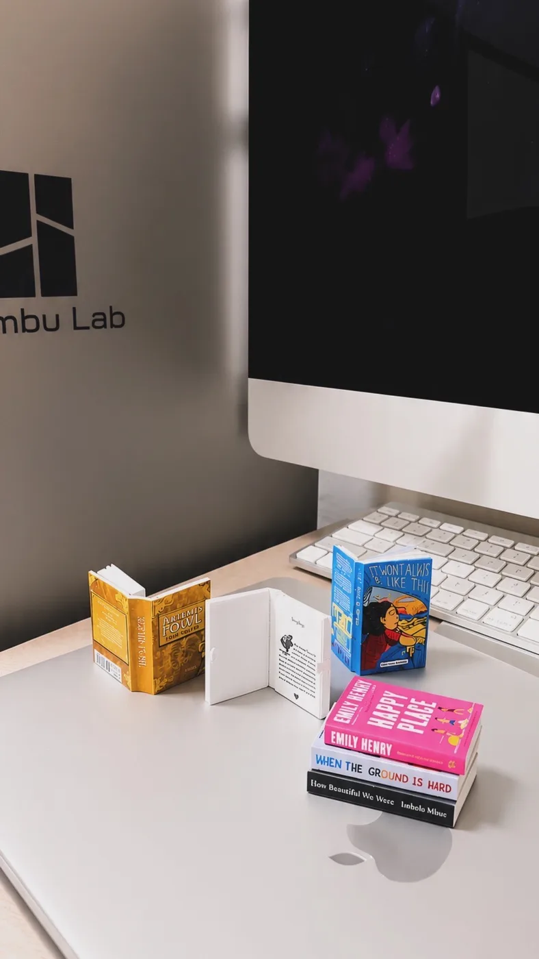 Miniature paperbacks on a working desk, one propped open, a stack topped with Happy Place