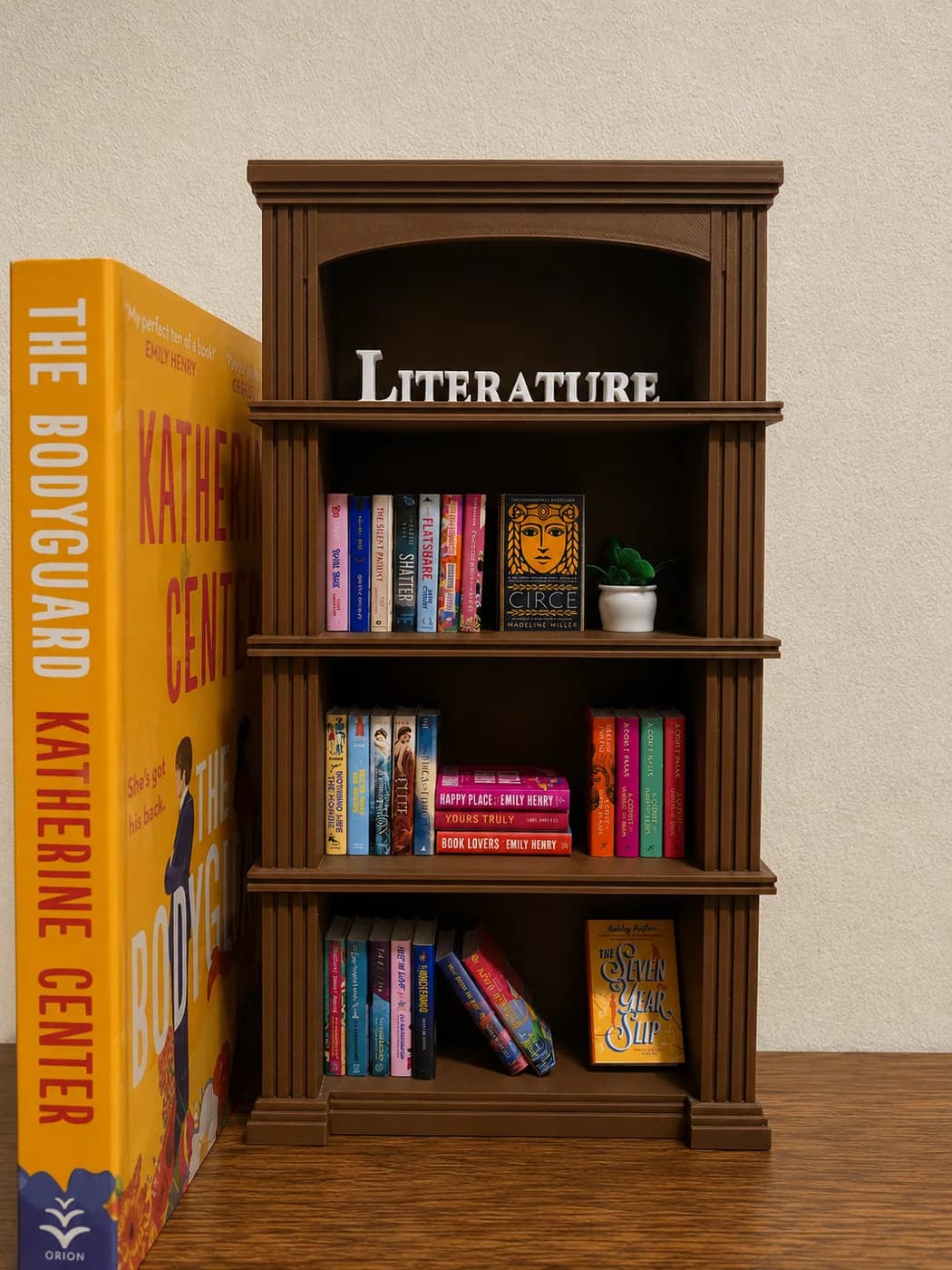 A choco brown Mini Classic bookshelf styled with tiny novels, a plant and white LITERATURE letters, standing next to a full-size hardback