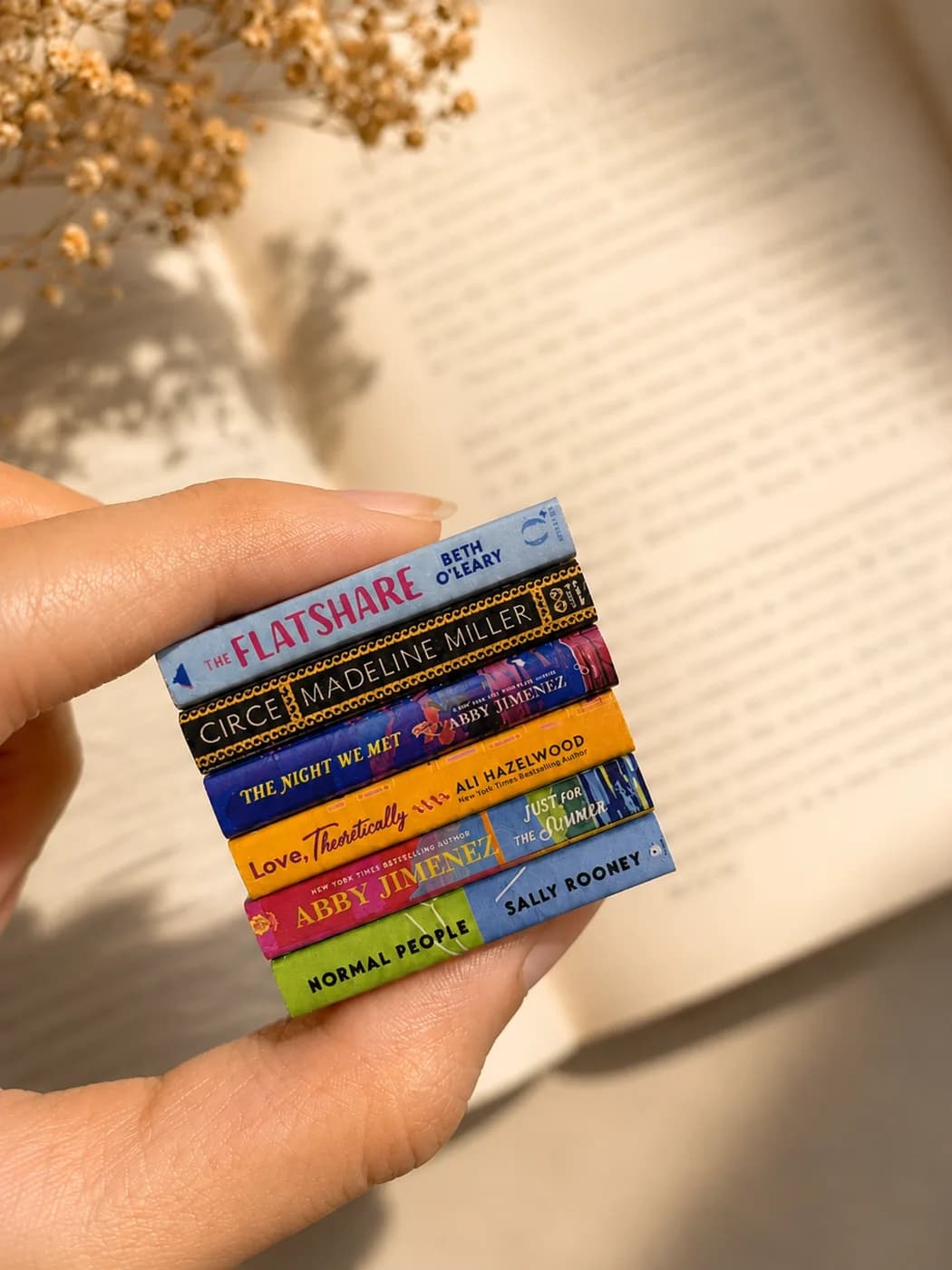 A hand holding a stack of six miniature novels, no longer than a thumb